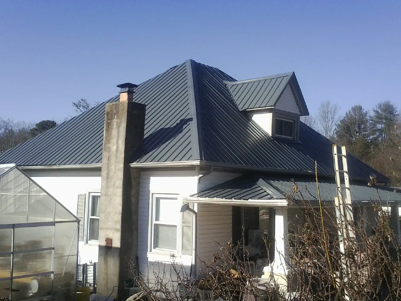 Dark blue standing seam metal roof on a white farmhouse with dormer — Slate & Tile Roof Repair by Roofing Brothers in Bonlee
