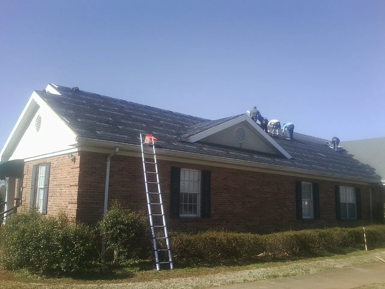 Crew tearing shingles off a brick ranch roof with a ladder set — Metal Roof Repair work by our crew in Bonlee