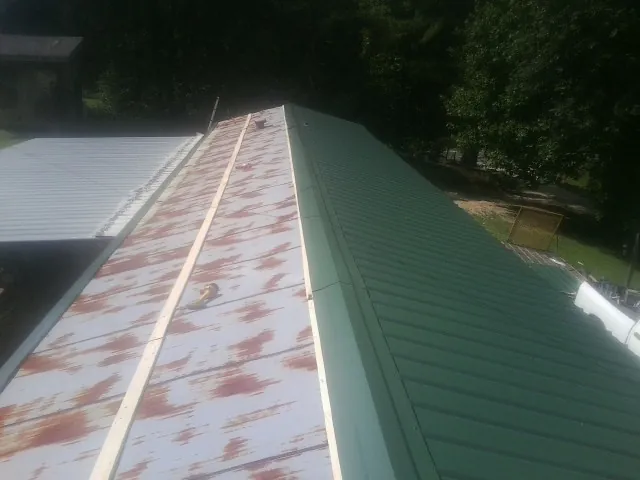 Old rusted panels beside newly installed green metal roofing — Wind Damage Roof Repair by Roofing Brothers in Bonlee