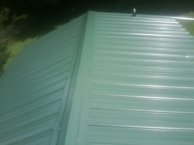 New green metal panels meeting at the ridge of a roof — Flat Roof Repair work by our crew in Bonlee