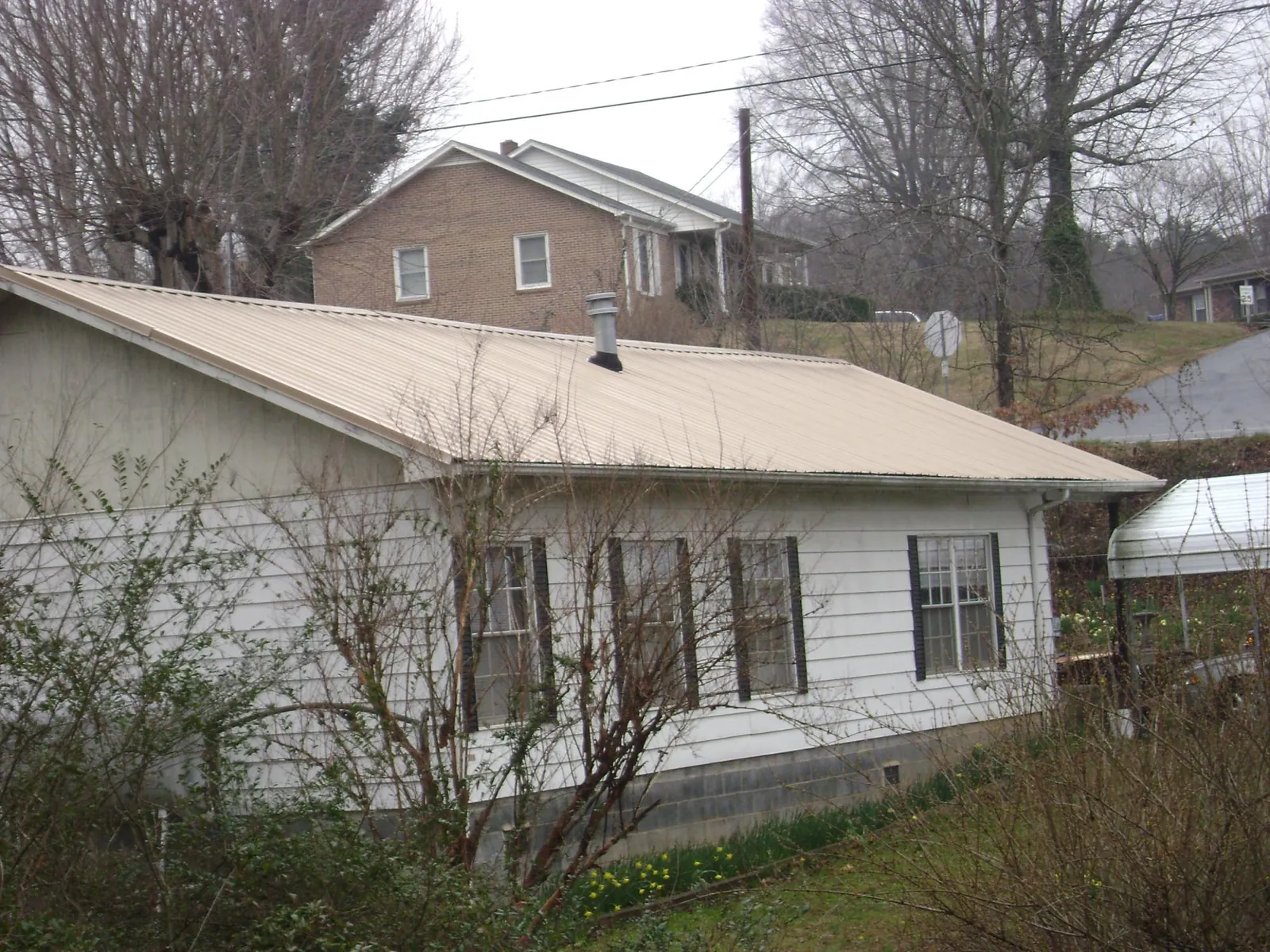 Tan metal roof on a white sided house set into a hillside — Commercial Roofing by Roofing Brothers in Bonlee