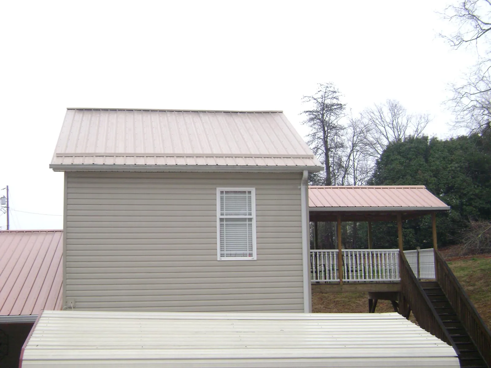 Tan metal roofs on a two story addition and attached porch, from a Roof Replacement job in Bonlee